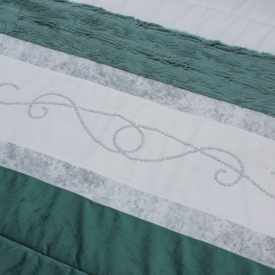 Têxtil para cama com faixas verdes, brancas e cinzentas e padrão de contas em espiral.