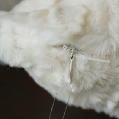 Produto felpudo branco com gancho de plástico transparente em fundo escuro