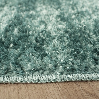 Tapete verde felpudo com borda costurada sobre chão de madeira clara