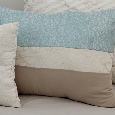 Conjunto de três almofadas decorativas em tons azul, bege e castanho claro sobre sofá.