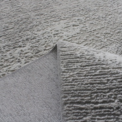 Tapete cinzento com textura elevada e padrão irregular, mostrando o verso