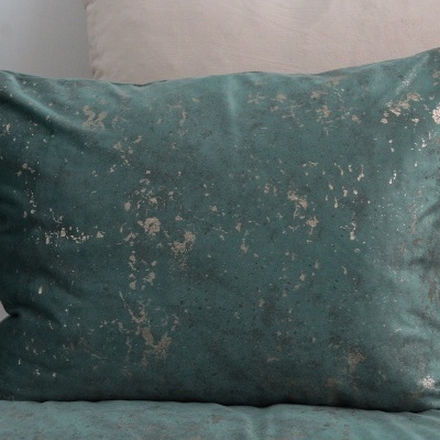 Almofada aveludada verde-azulada com manchas douradas sobre almofada bege