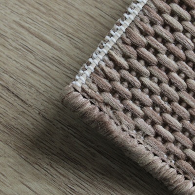 Detalhe de tapete castanho claro e bege com borda branca sobre chão de madeira clara