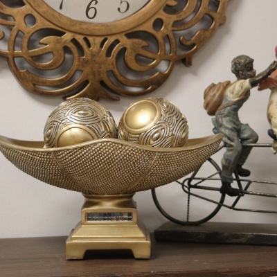 Decoração dourada com bolas texturizadas e base, junto a figura de menino com mochila