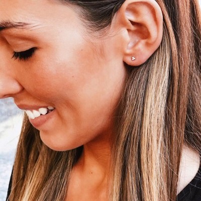 Mulher com brinco pequeno dourado em forma de flor no lóbulo da orelha esquerda
