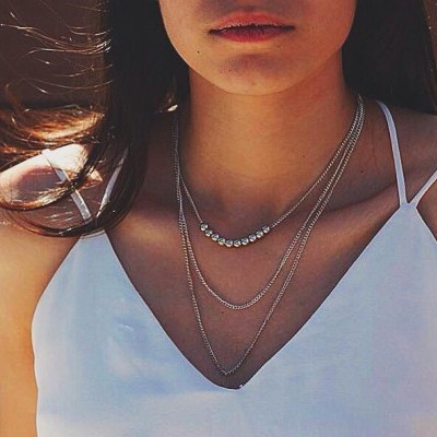 mulher com top branco e três colares prateados