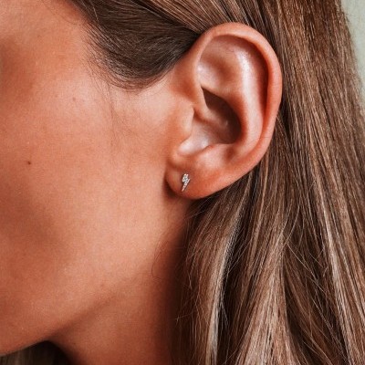 Brinco pequeno de raio prateado na orelha de uma pessoa