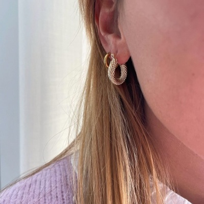 Brinco de argola dourado com textura trançada usado por pessoa com cabelo loiro