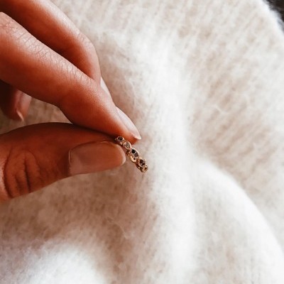 anel dourado fino com detalhes em relevo numa mão sobre tecido branco felpudo