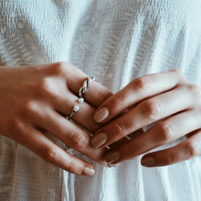 Mãos femininas com anéis prateados e fundo branco texturizado