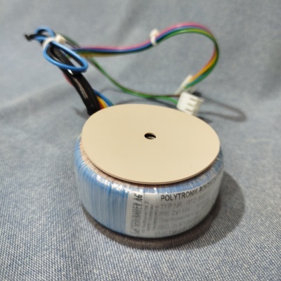 Transformador toroidal com fios coloridos e conector branco sobre tecido cinza