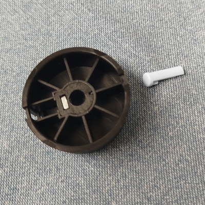 Peça plástica redonda preta com parafuso branco sobre tecido azul claro