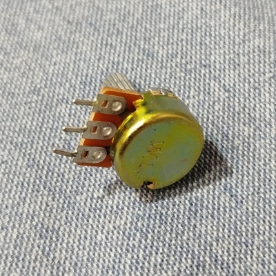 Potenciómetro metálico com três terminais sobre tecido azul escuro listrado