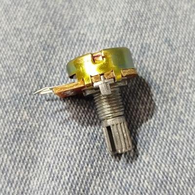 Potenciômetro metálico com corpo dourado e pino de solda sobre tecido azul