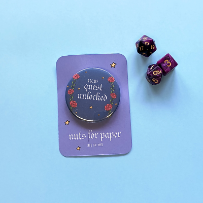 Chapa decorativa com texto 'quest unlocked' e dois dados de jogo em fundo azul