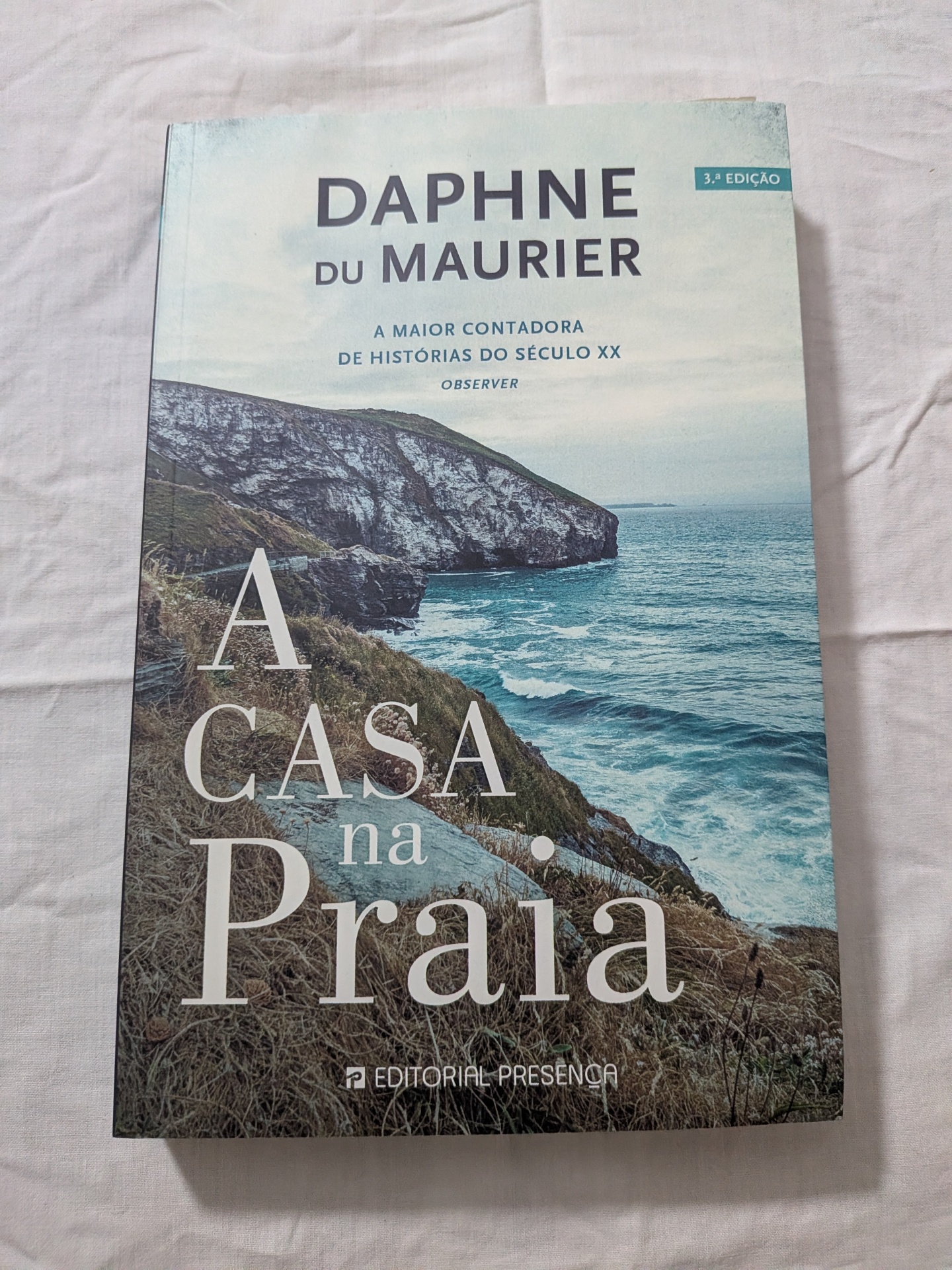 Daphne Du Maurier - A Casa na Praia Livro com capa de penhascos e mar, título 'A Casa na Praia'.
