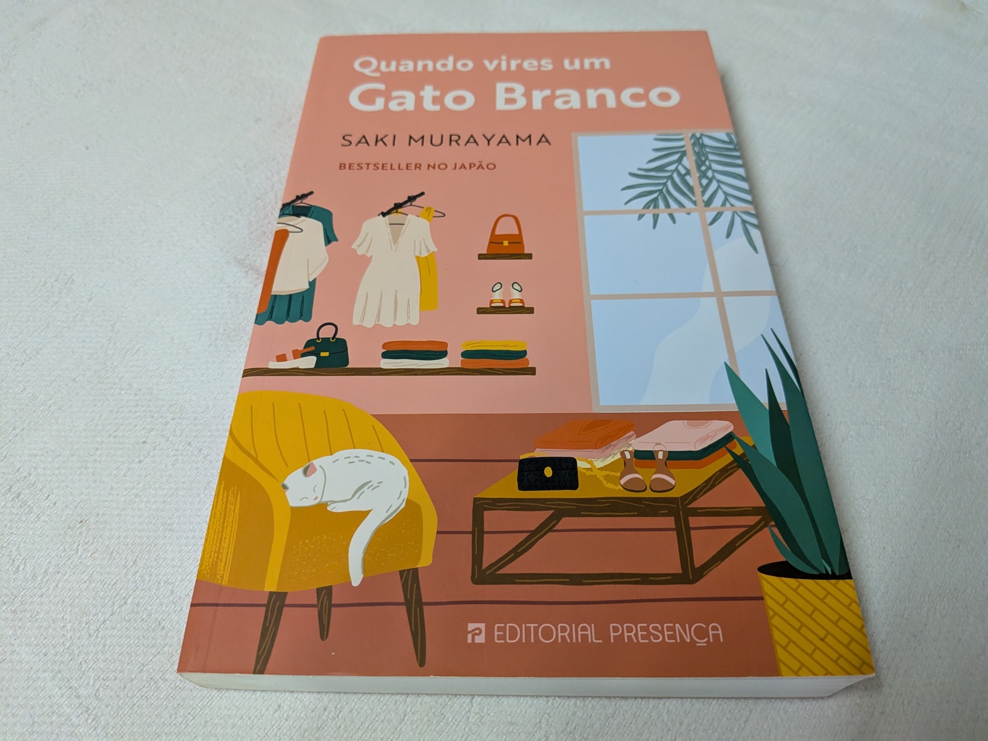 Saki Murayama - Quando Vires um Gato Branco Livro 'Quando vires um Gato Branco' com capa rosa, cadeira amarela e gato branco desenhados.