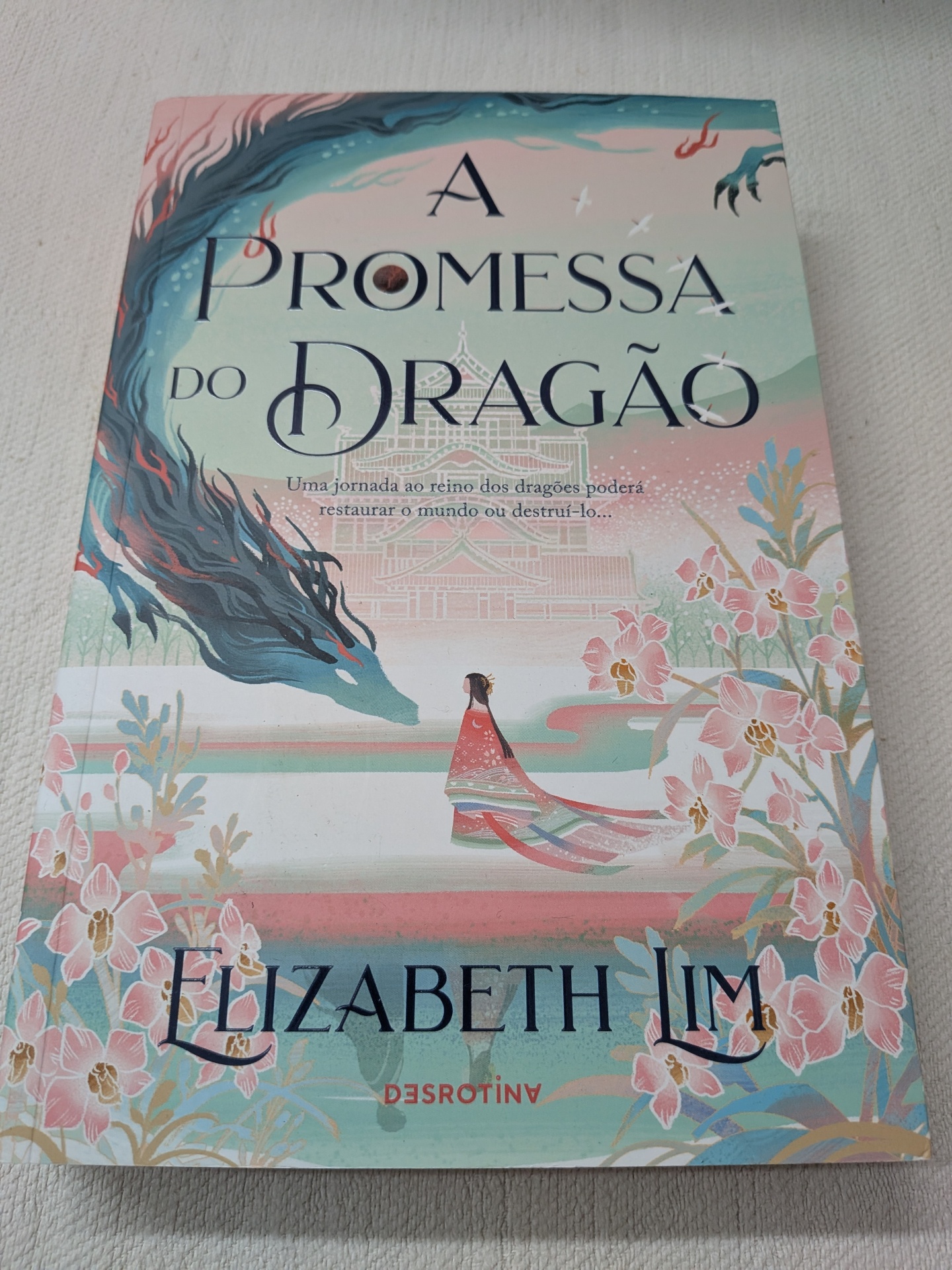 Elizabeth Lim - A Promessa do Dragão Capa do livro 'A PROMESSA DO DRAGÃO' com ilustração de dragão azul, mulher em kimono vermelho e flores cor-de-rosa.