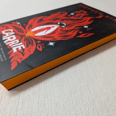 Livro 'Carrie' de Stephen King com capa preta, ilustração vermelha e branca, e laterais amarelas