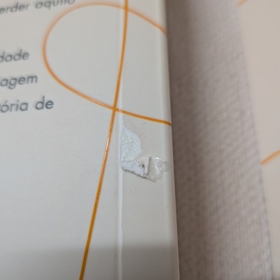 Produto em embalagem branca com linhas laranja e texto em português com etiqueta rasgada colada