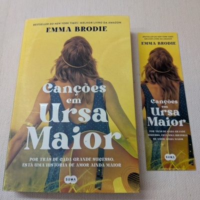 Livro e marcador de livros Canções em Ursa Maior de Emma Brodie com capa amarela e mulher de costas