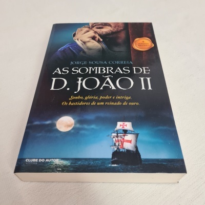 Capa do livro 'As Sombras de D. João II' com imagem de homem, navio no mar e lua cheia