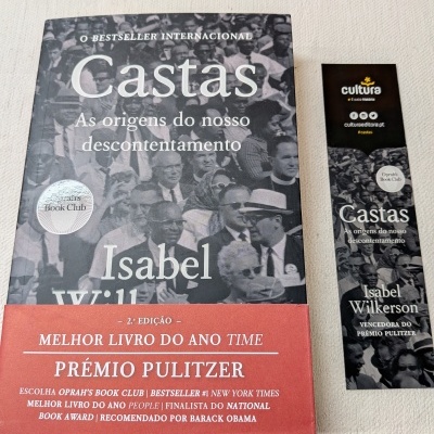 Livro 'Castas' de Isabel Wilkerson com faixa vermelha e marcador de livro correspondente ao lado.