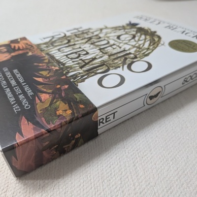 Livro com capa branca e ilustração dourada de gaiola, faixa colorida e texto promocional em português