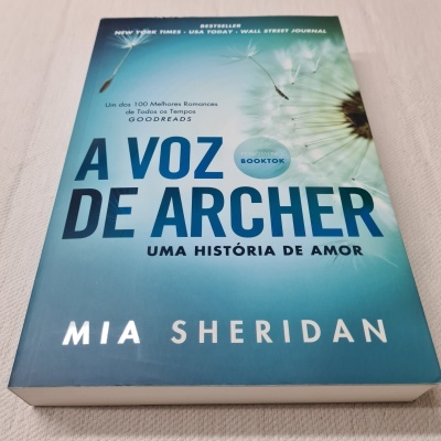 Livro A Voz de Archer com capa azul e sementes de dente-de-leão