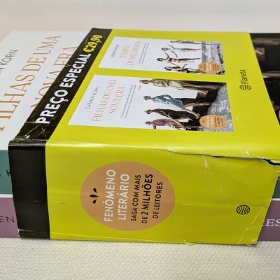 Conjunto de dois livros com capa dura e embalagem promocional amarela com texto, sobre uma superfície clara.