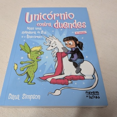 Capa de livro azul com ilustração de duende verde, unicórnio branco com cabelo rosa e menina de cabelos castanhos escuros