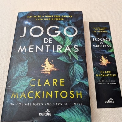 Capa do livro 'Jogo de Mentiras' com folhas verdes e fogueira e marcador de página correspondente.