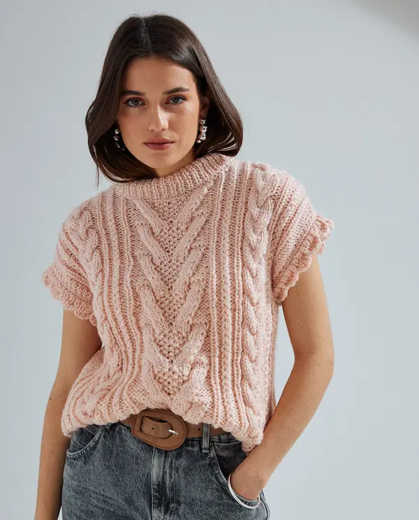 Mulher vestindo top de malha rosa com padrão trançado e jeans cinzentos com cinto castanho.