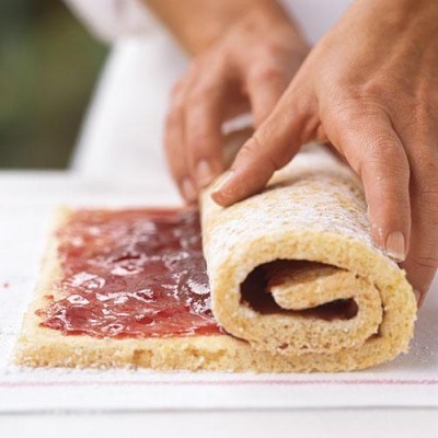 Mãos a enrolar bolo esponjoso com compota de morango