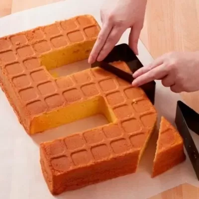 Bolo amarelo em forma de número 5 com textura quadriculada, cortado na bancada de cozinha