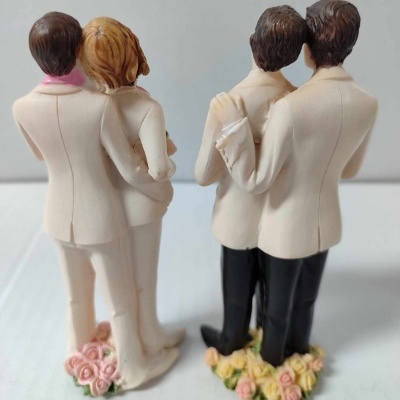 Figuras em resina de dois casais, um masculino e outro heterossexual, com roupas brancas e bases florais.