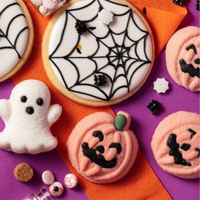 Biscoitos decorados de Halloween com teias de aranha, abóboras e fantasma, em fundo roxo e laranja