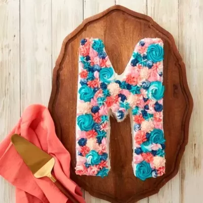 Bolo letra M decorado com flores coloridas em tábua de madeira