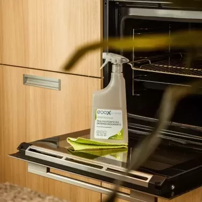 Frasco de produto de limpeza multiusos EOXX e pano verde sobre porta aberta de forno preto