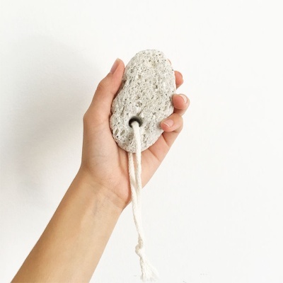 Mão a segurar pedra-pomes branca com cordão de algodão em fundo branco.