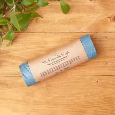 Rolo de sacos de plástico reciclado azuis com embalagem de papel castanho sobre madeira clara