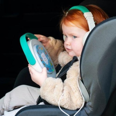 Criança ruiva usa headphones e segura dispositivo colorido sentada em cadeira com cinto