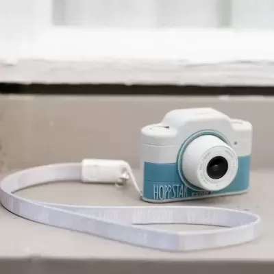 Máquina fotográfica de brincar azul e branca com correia branca em superfície junto a janela