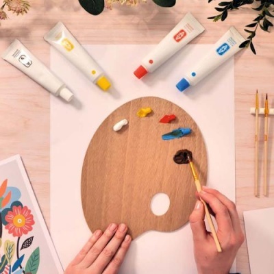 Paleta de madeira com tintas primárias, pincéis e papel decorativo floral