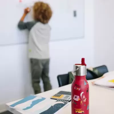 Garrafa térmica vermelha decorada numa mesa branca com criança ao fundo