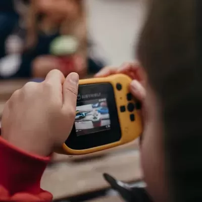 Consola portátil amarela de videojogos nas mãos de uma criança em ambiente interior.