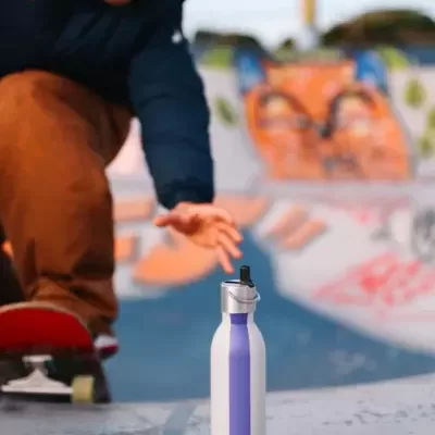 Garrafa reutilizável branca com faixa roxa numa superfície de skate