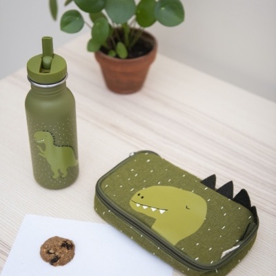 frasqueira e garrafa verdes com estampa de dinossauro, lápis e bolacha sobre mesa de madeira