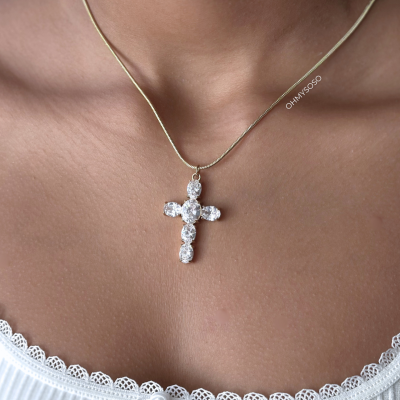 Colar dourado com pendente de cruz de pedras brilhantes num pescoço com topo branco de renda