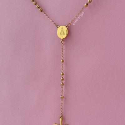 Colar dourado com contas e cruz pendurada sobre fundo rosa